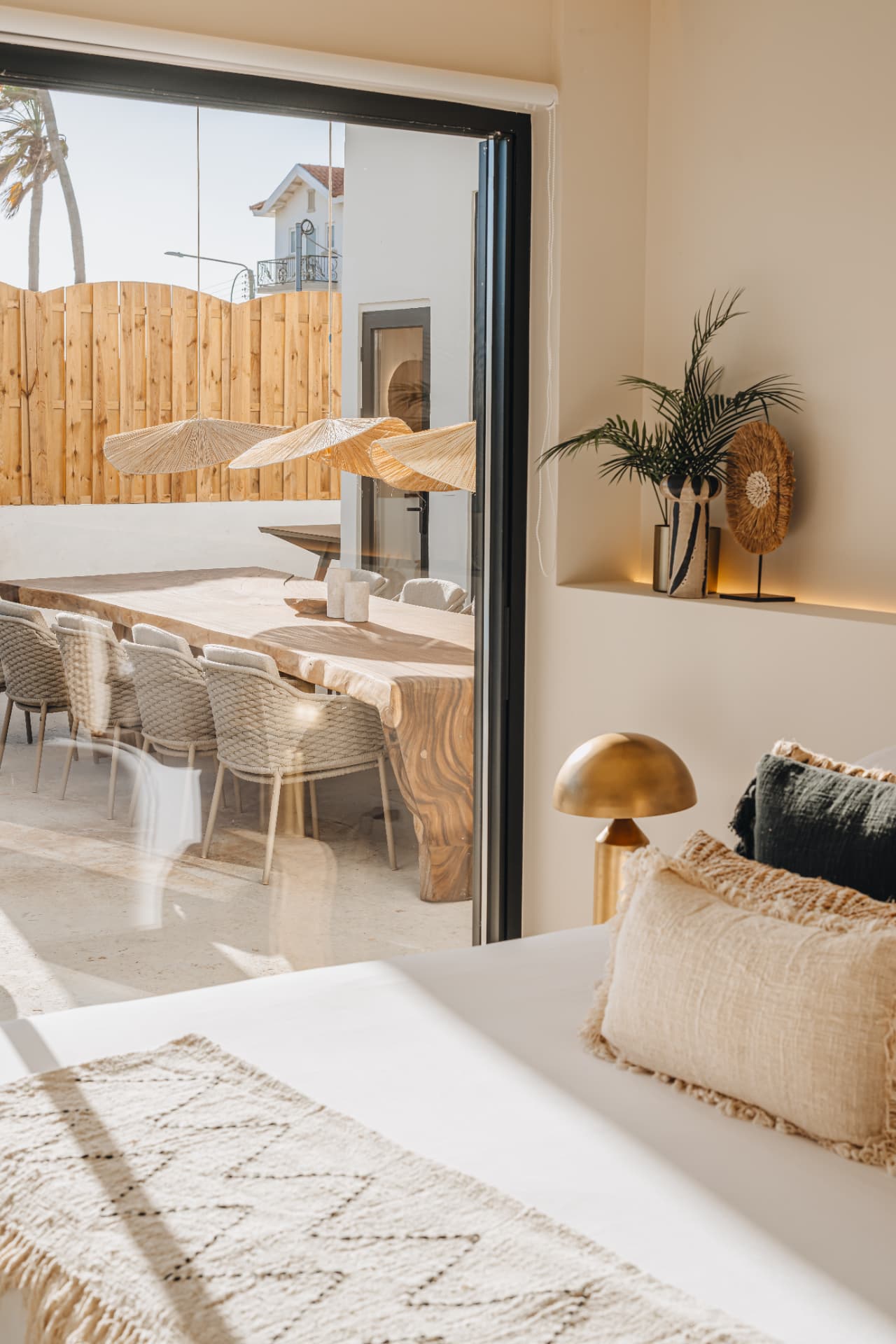 Indoor dining area opening onto a shaded patio with a long wooden table and woven chairs