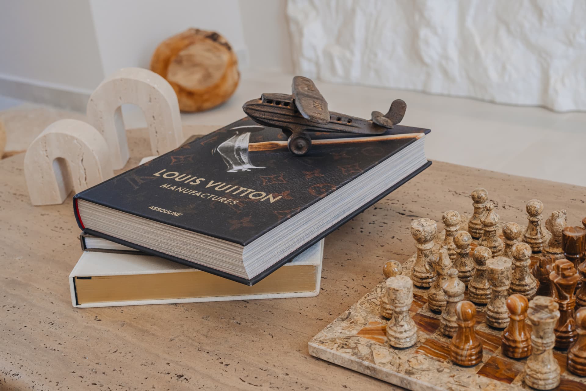 Marble coffee table styled with a Louis Vuitton book, stone chess set and sculptural objects