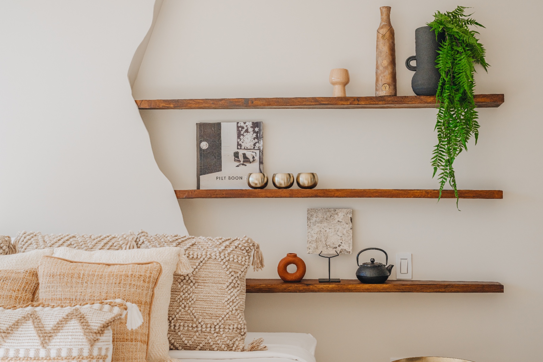 Wood shelves styled with linen cushions, ceramics and a fern