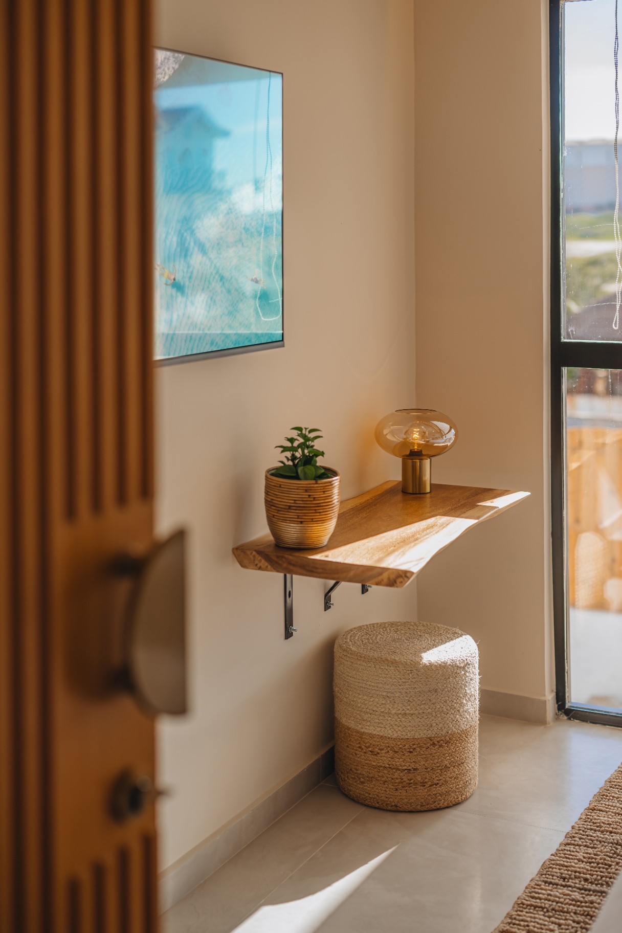 Quiet entryway with a wooden shelf, warm lamp and jute pouf in morning light